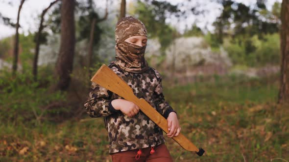 Portrait of Young Ukrainian Boy in Camouflage and in Balaclava with Wooden Gun