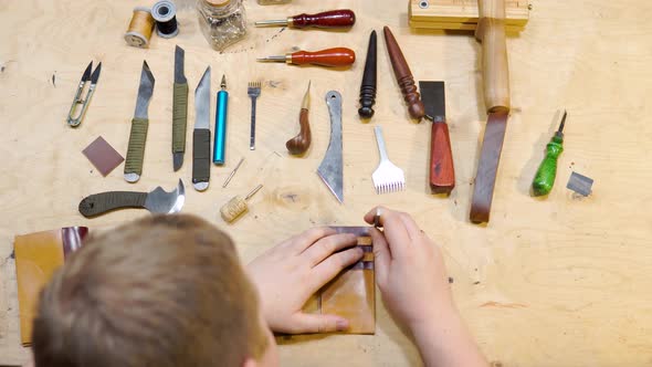 Close-up of Male Master Cutting Piece of Leather with Crafting Tools for Future Wallet at Workshop alt