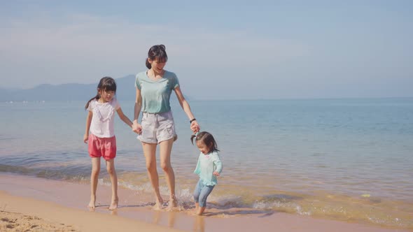 Asian family on vacation. Beautiful mother feeling relax playing on the sand sea with kid children. alt