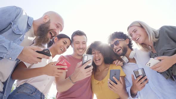 Low Angle of Multiracial Happy Group of Friends Using Phone and Smiling Together Outside alt
