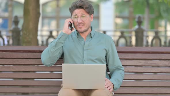 Middle Aged Man Talking on Phone while using Laptop alt