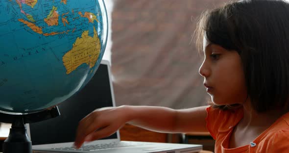 Little girl looking at globe in classroom alt
