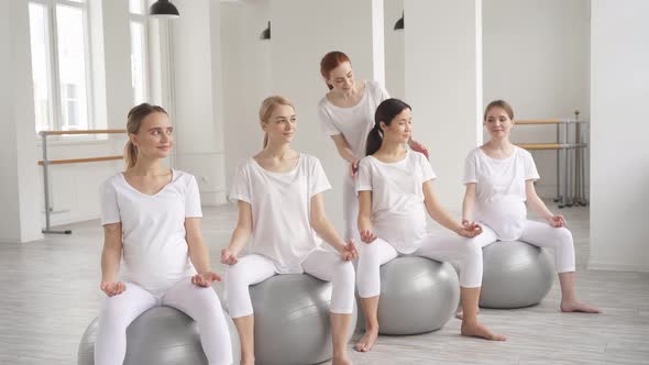 Gravid Women Taking Yoga Class From Female Personal Fitness Coach Who Helps to Do Exercises