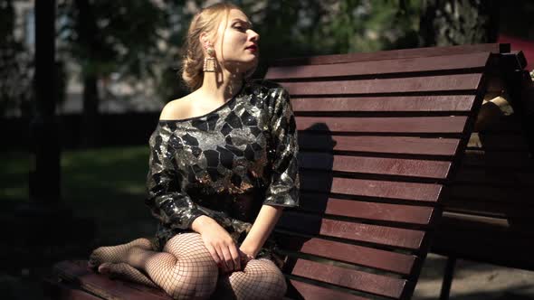 Barefoot Caucasian Young Woman in Party Dress on Bench in Park Standing Up Looking Away alt