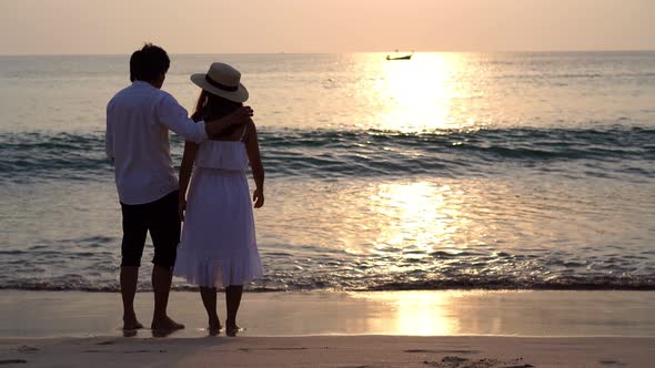 Young asian couple looking beautiful sunset on the beach