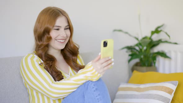 Woman sitting on couch, having video call over smartphone