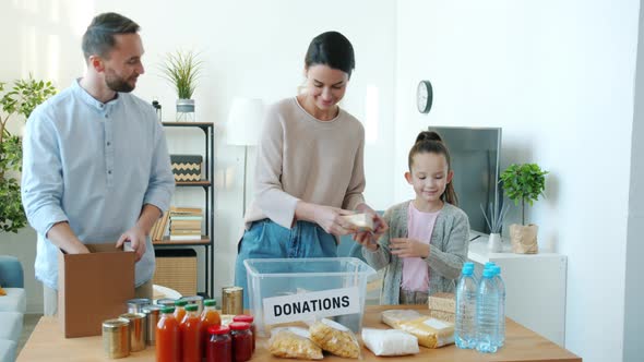 Mom Dad and Kid Packing Food Products for Donation Helping Poor Indoors in Apartment alt