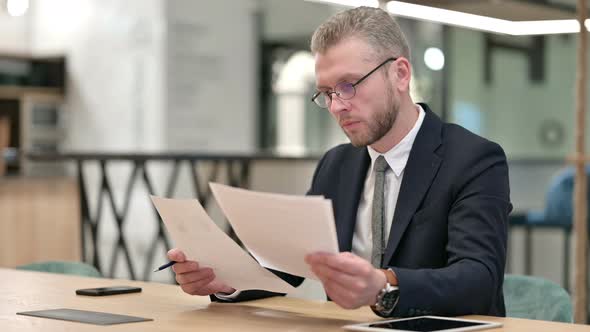 Hardworking Businessman Reading Documents in Office  alt