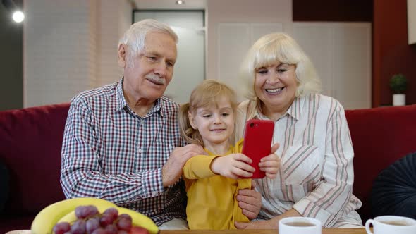 Senior Couple Grandparents with Child Granddaughter Making Selfie Photos Together on Mobile Phone alt