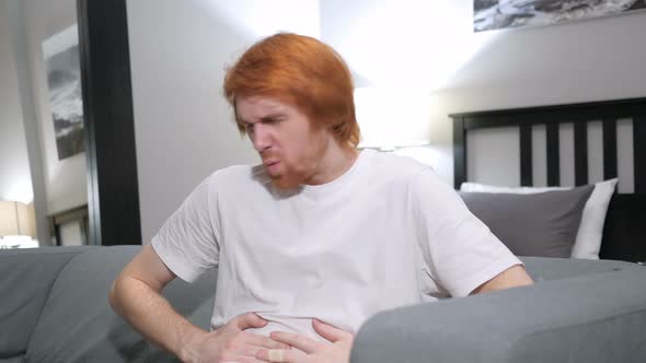 Redhead Man with Abdominal Pain Sitting on Couch in Bedroom alt