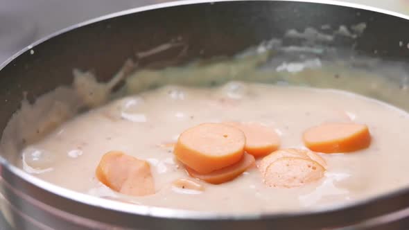 Close-up of a woman's hand putting a small piece of sausage in Carbonara Mushroom Sauces. alt