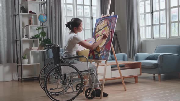Asian Artist Girl In Wheelchair Holding Paintbrush Mixed Colour And Painting A Girl On The Canvas alt