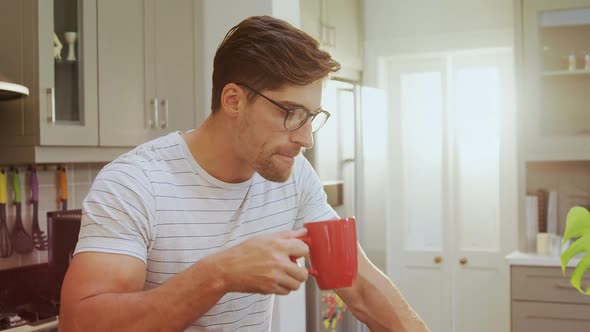 Young man wearing spectacles sitting on stool having coffee while using laptop 4K 4k alt