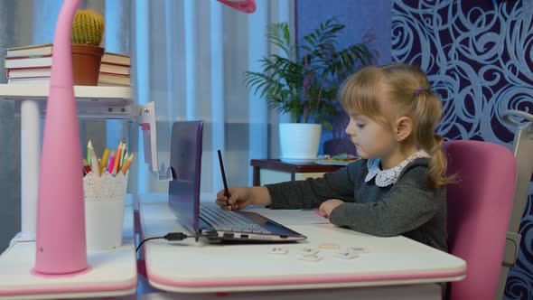Child Schoolgirl Learning Lessons Distance Education at Home Sitting at Table Using Laptop Computer alt