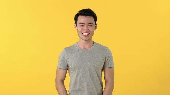 Happy young Asian man in gray t-shirt laughing isolated on yellow studio background