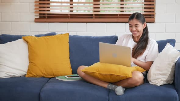 Young Asian woman successful happy cheerful smiling using laptop on a sofa in the living room.