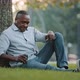 Elderly African Man Businessman Entrepreneur Sitting on Grass Resting Next to Tree in City Park - VideoHive Item for Sale