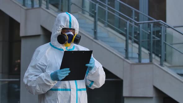 A Portrait of a Young Man in a Protective Suit, Respirator, Gloves and Safety Glasses Holds a Folder alt