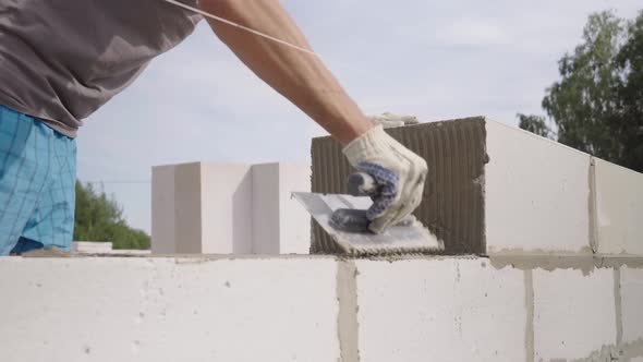 bricklayer laying wall from a block, with a spatula for putty in the open air. alt