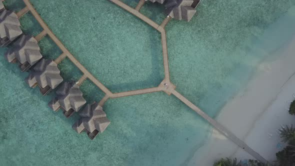 Aerial view of man and woman lovers couple lie on wooden boardwalk near luxury bungalows, Maldives
