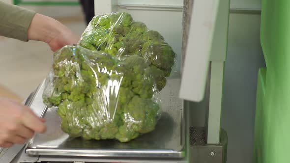 Closeup of a Woman Weighing Broccoli on Scales in a Supermarket alt