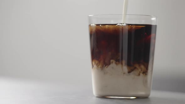 Slow Motion Pour Cream in Cola in Tumbler Glass on Concrete Countertop with Copy Space alt