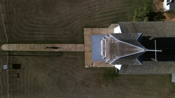Lonely person walking along narrow path towards old wooden country church in American prairie. Top-d alt