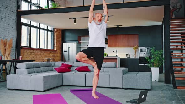 Man in White Tshirt and Black Shorts Doing Yoga Excercises on a Pink Mat in Living Room in Front of alt