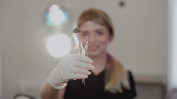 Young attractive blonde female dentist with a smile shows dentist tools to the camera.