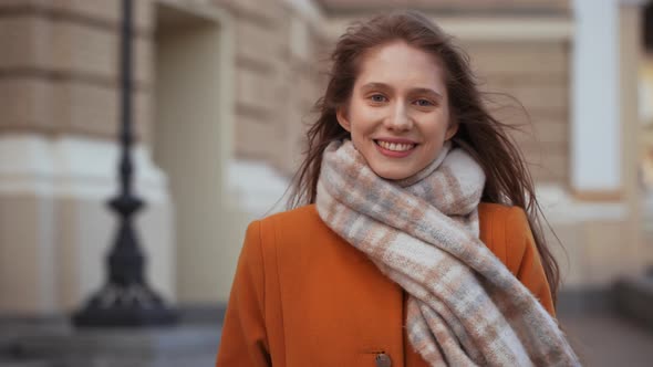 Portrait of Cute Caucasian Woman Wearing Coat and Scarf Looking at Camera with Smile While Standing alt