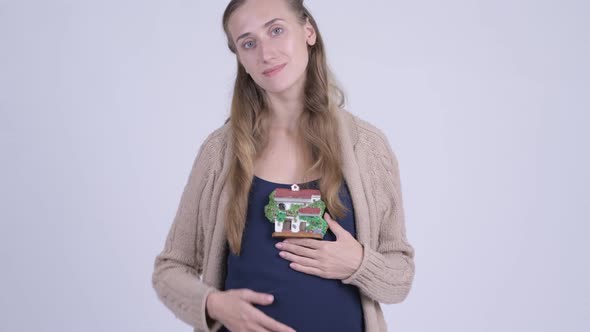 Happy Young Pregnant Woman Holding House Figurine alt