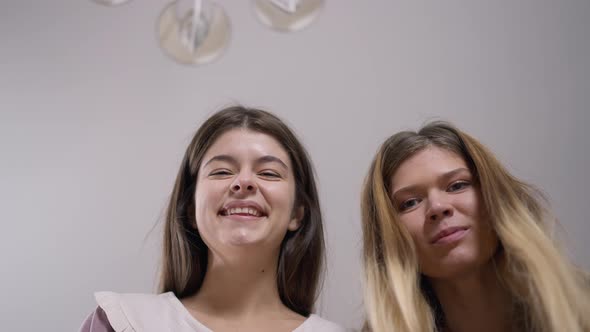 Closeup Two Cheerful Women Looking at Camera Laughing Out Loud with Ceiling at Background alt