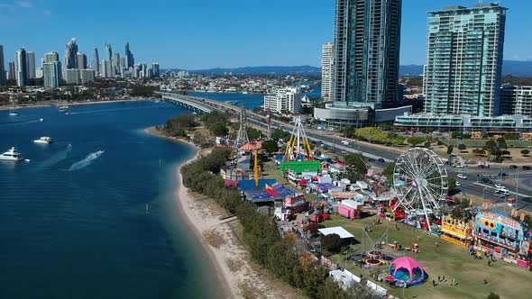 Aerial view of a colourful carnival situated by the sea with a city skyline in the background alt