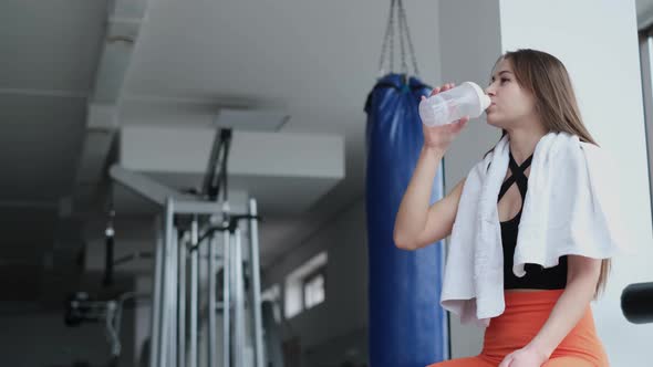 Fitness Woman Drinking Water While Sitting in the Gym alt