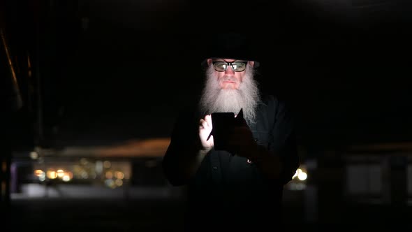 Mature Bearded Man Looking Suspicious While Using Phone in the Dark