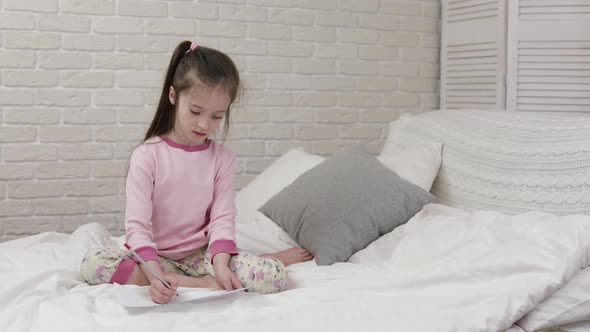 Cute Little Girl Drawing Pictures While Lying on Bed