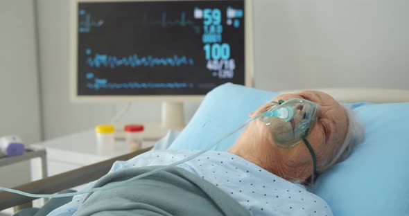 Ill Senior Woman Lying in Hospital Bed While Wearing an Oxygen Mask alt