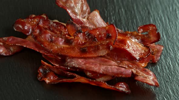 Super Slow Motion Shot of Roasted Bacon Slices Falling on Black Table at 1000 Fps. alt