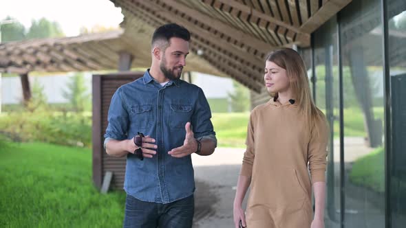 Two young people - a man and a woman are walking in the park, talking alt
