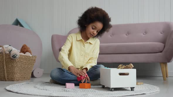 Little African American Girl Builds Tower From Colored Wooden Construction Kit alt