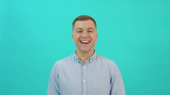 Positive Middleaged Man in a Blue Shirt Looks Into the Camera and Laughs Out Loud on a Bright Blue alt