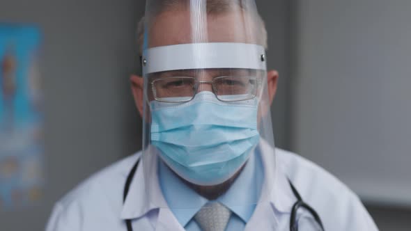Portrait of Male Doctor in Glasses Wearing Transparent Protective Face Shield Mask in Hospital Room