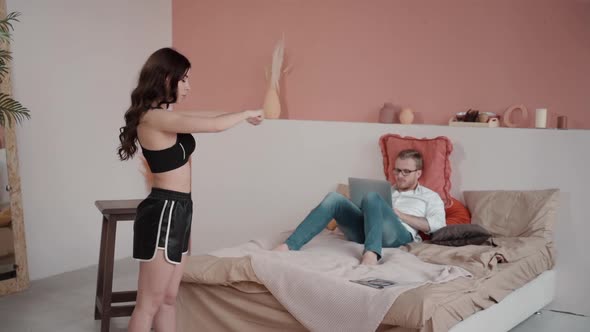Girl Exercising, Practicing Sport at Home As Her Boyfriend Man Is Surfing Laptop on Bed. Woman