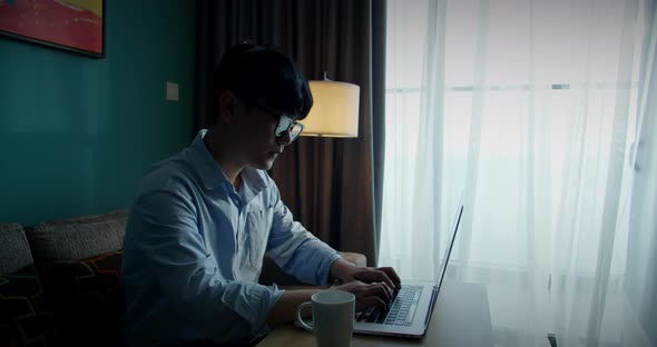 Young Attractive Asian Vietnam Man Busy Work Computer or Smart Tablet on Laptop at Home in Freelance alt