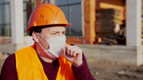 Male Construction Worker in Overalls and Medical Mask Coughing on Background of House Under