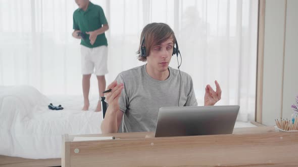 Young father working on laptop computer and son playing naughty at home, dad video call conference. alt