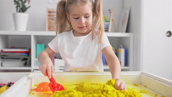 Little blonde girl with two ponytales play with magic sand.