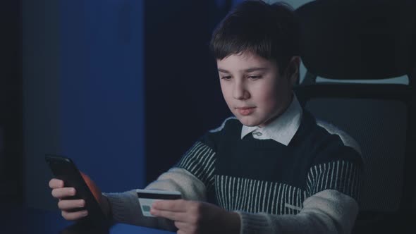 12-13 Years Old Boy Shopping Online with Credit Card and Smartphone While Sitting at Home Late at alt