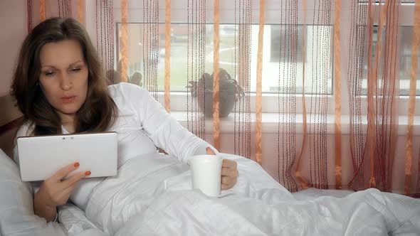 Worried Woman Reading Bad News in Tablet Computer and Drink Morning Coffee Tea