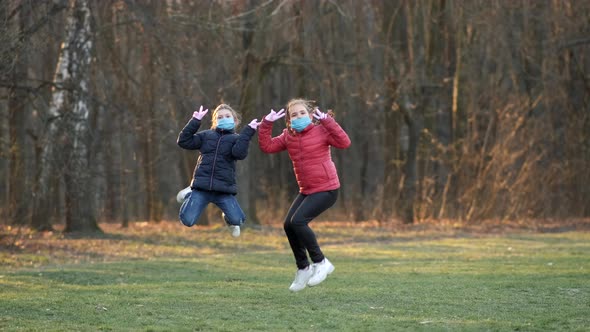 Two Little Girls Wearing Medical Masks Jump in a Spring Park. Slow Motion. The Concept of Protection